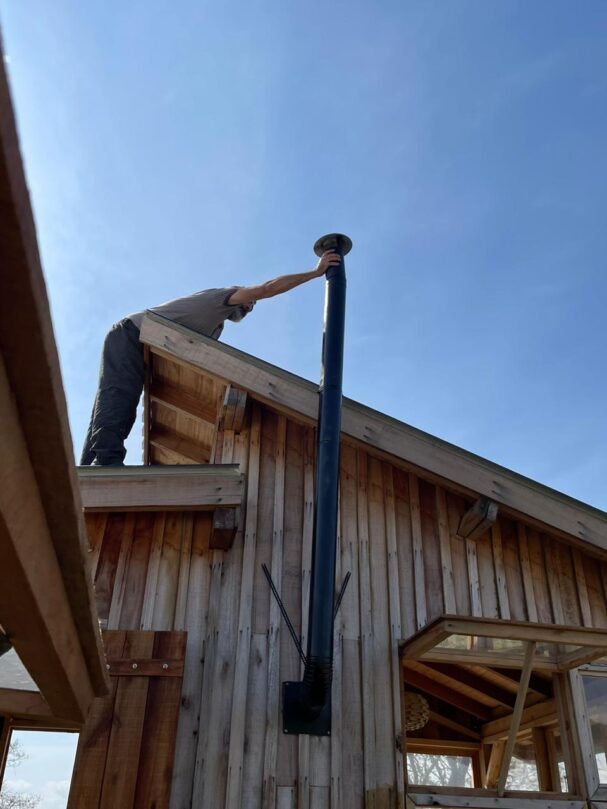 Installing wood stove chimney on tiny cabin roof during construction