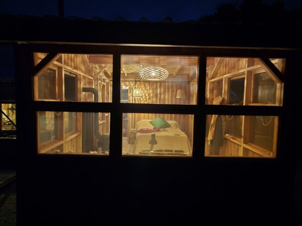 Tiny cabin interior at night with wood stove and warm lighting